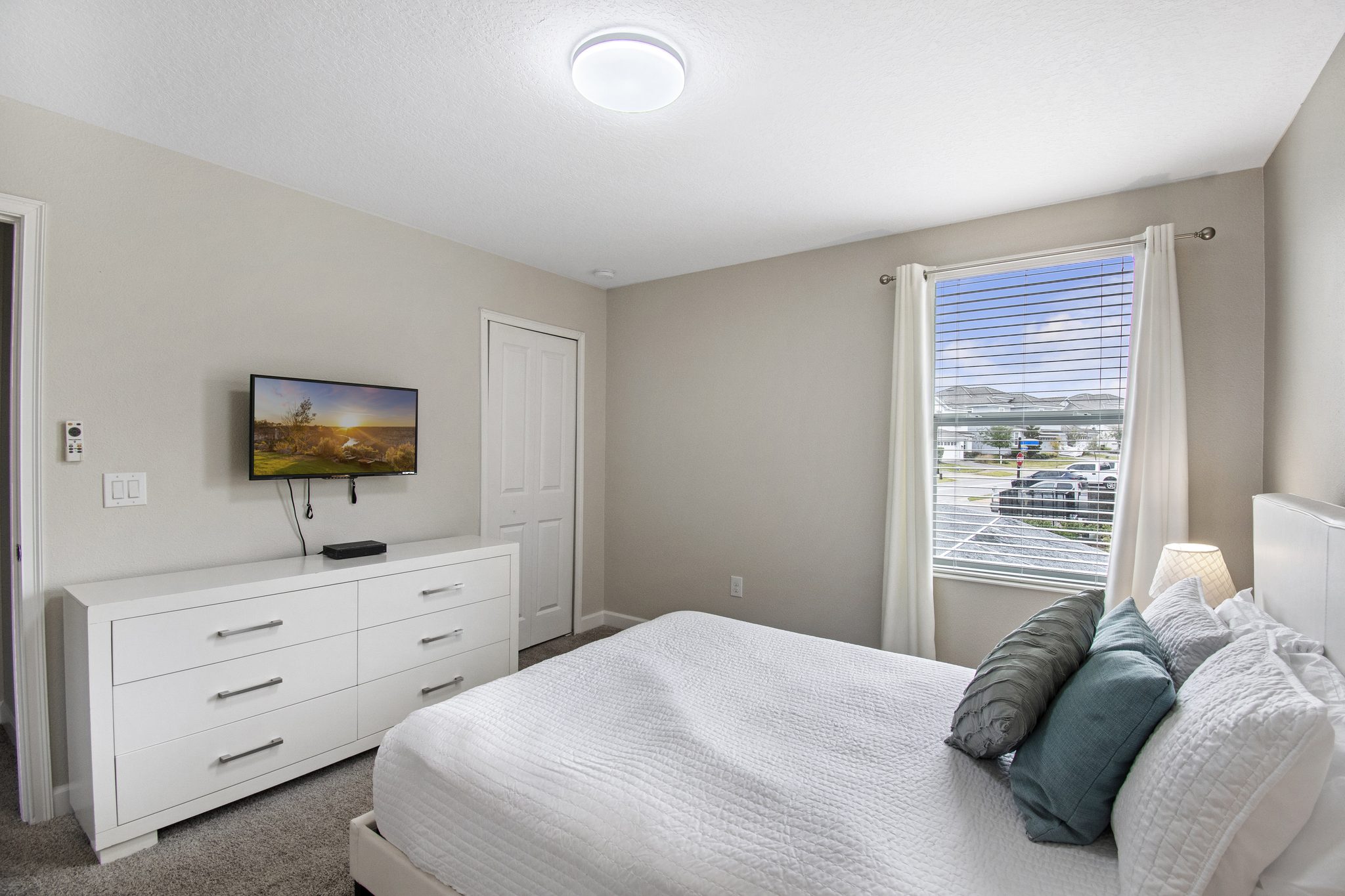 Bedroom with a queen bed, white dresser, wall-mounted TV, and window