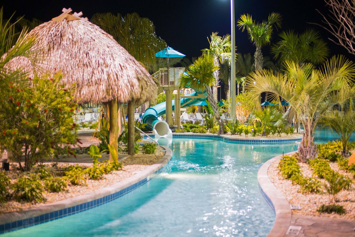 The Oasis Club lazy river and water slide lit up at night — resort access is inc