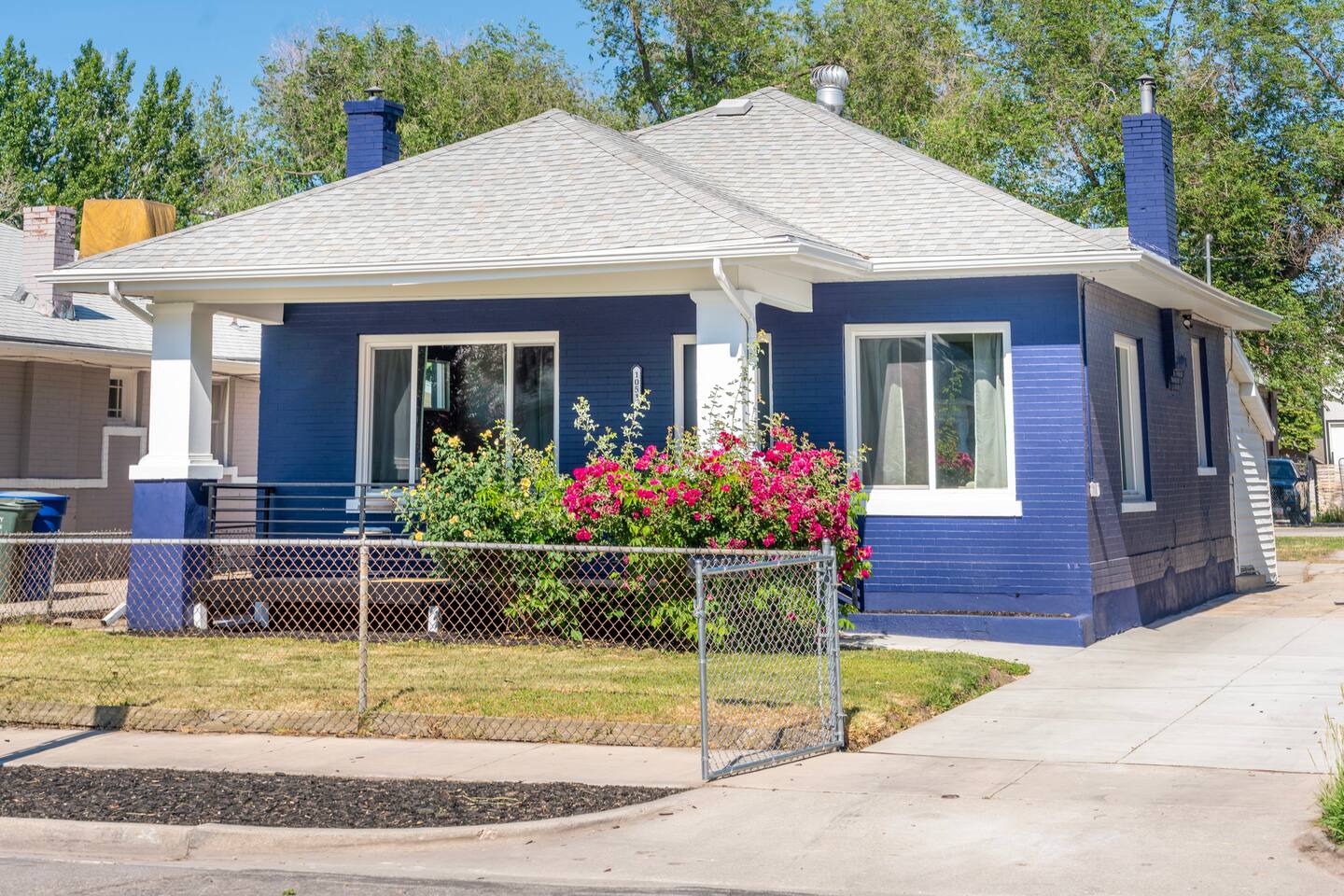 Freshly painted navy-blue brick bungalow on a fenced corner lot, framed by bloom