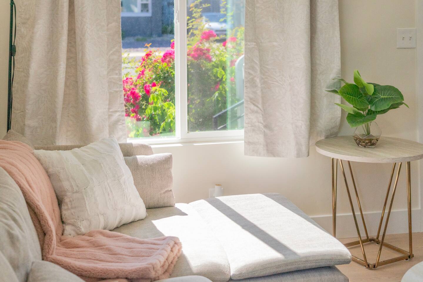 Sunlit sitting area with a cozy sofa, plush throw pillows, and a garden view out