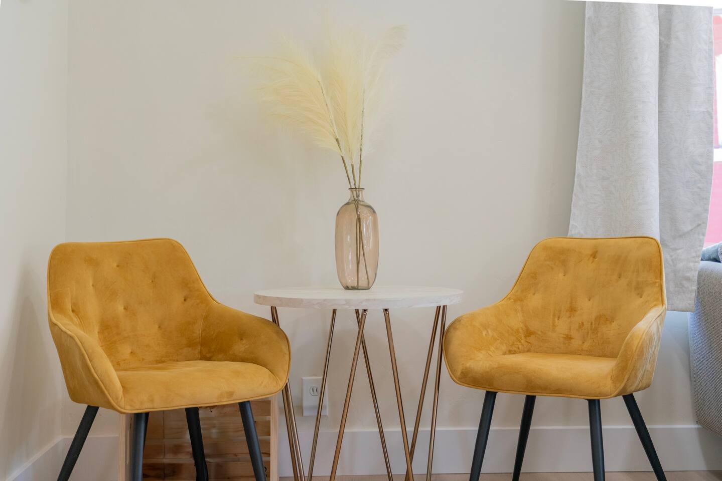 A pair of mustard velvet accent chairs and a marble-top side table make a bright