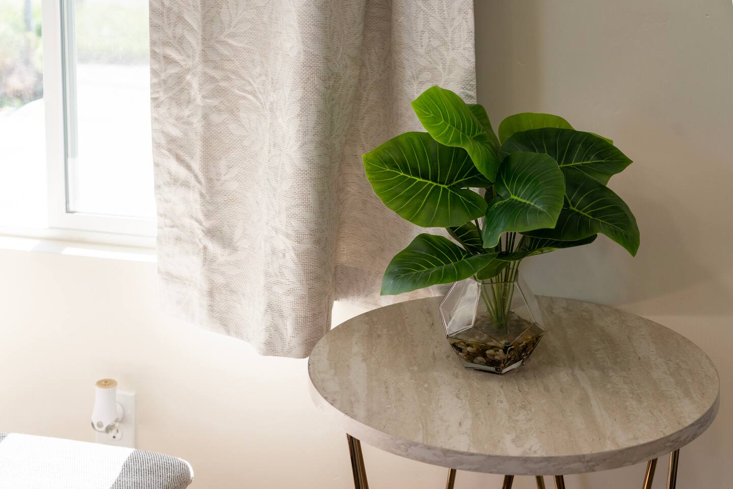 Decorative greenery in a glass vase on a marble side table beside a curtained wi