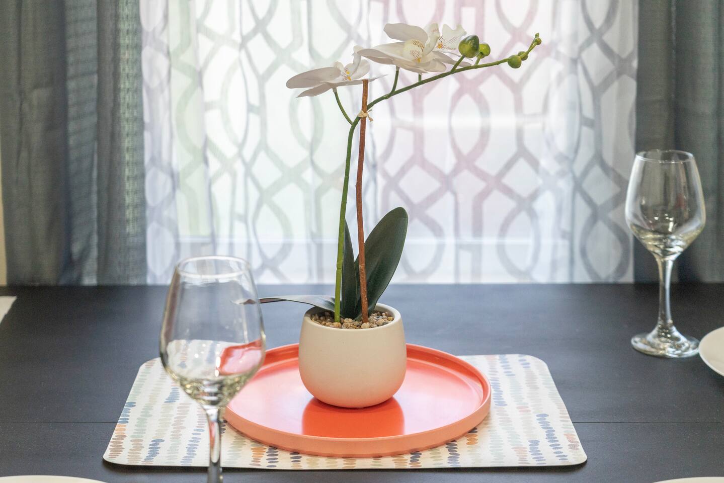 Dining table centerpiece with a potted orchid on a coral tray and wine glasses.
