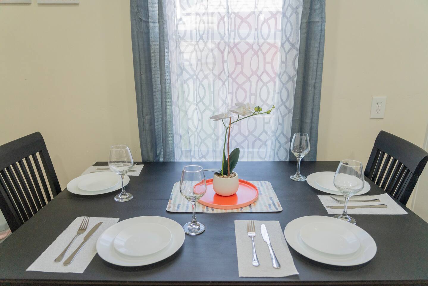Dining table set for four beside a curtained window.