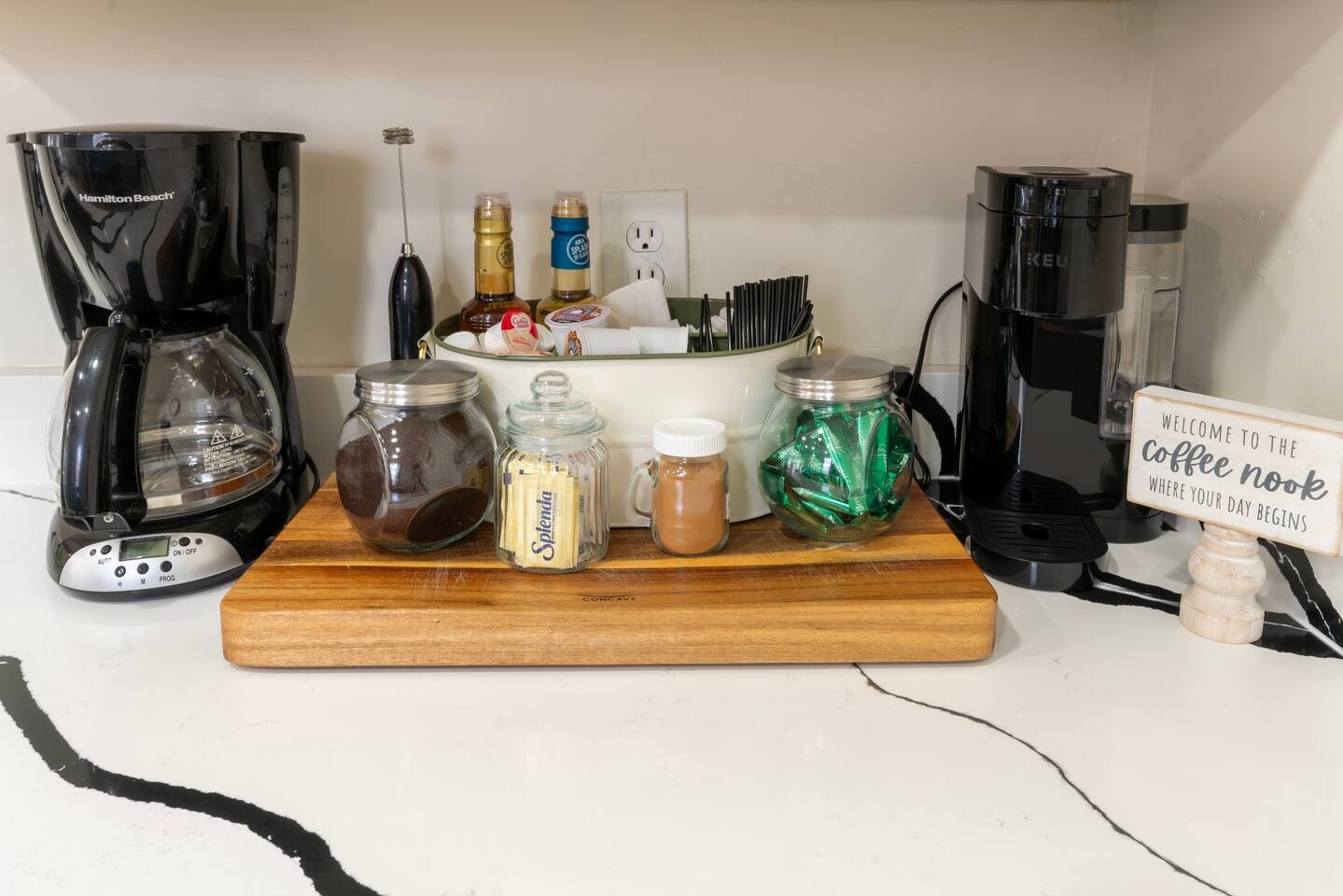 Coffee bar with drip and Keurig machines plus jars of coffee, sweeteners, and cr