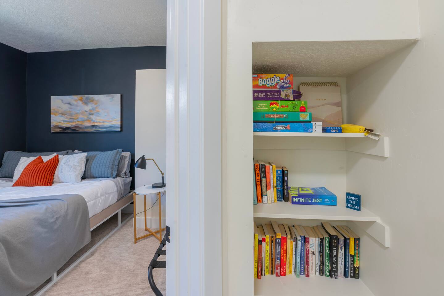 Bedroom with a king bed and a built-in shelf stocked with books and board games.