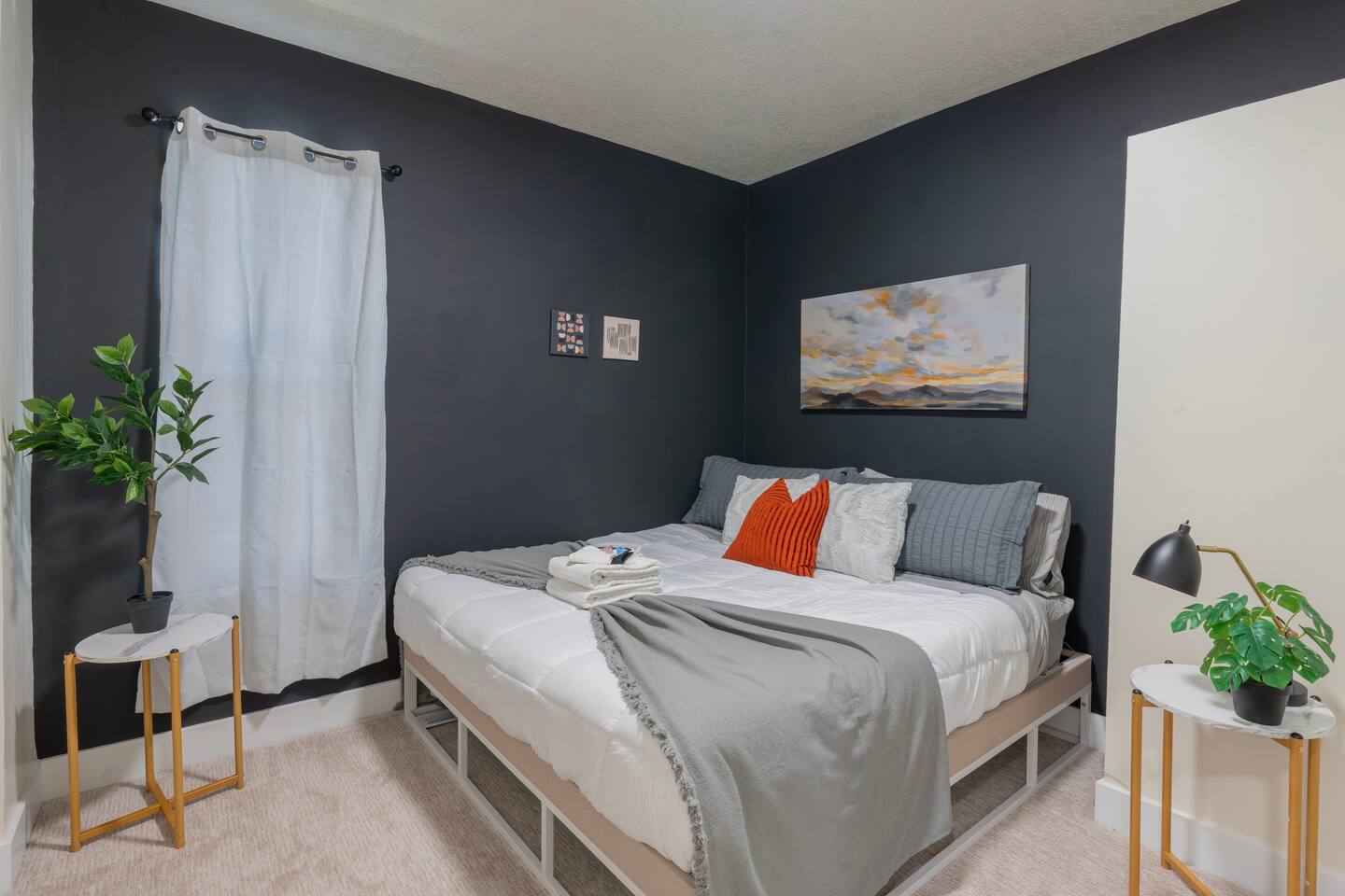 King bedroom with a charcoal accent wall, sunrise landscape artwork, and potted 