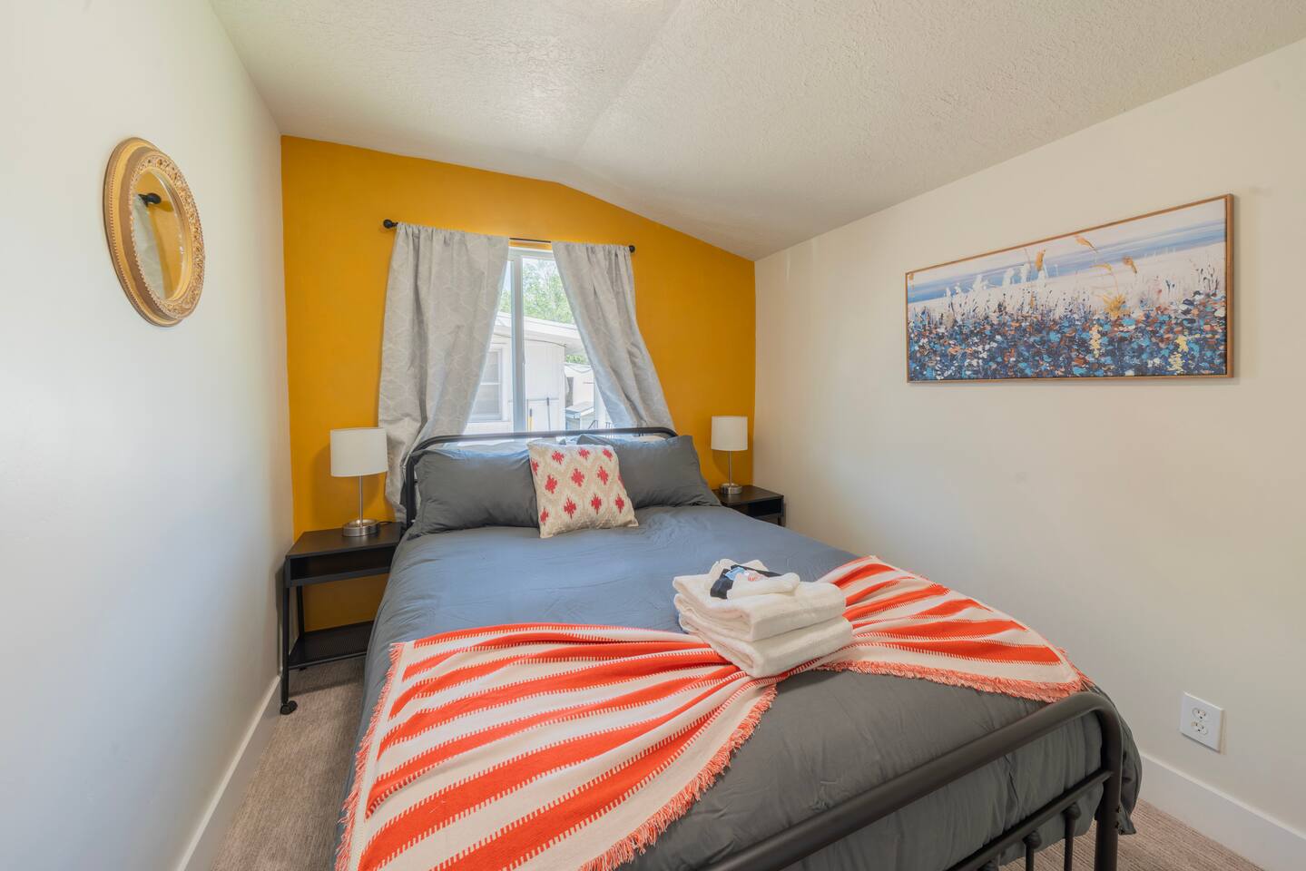 Bedroom with a queen bed, sunny yellow accent wall, and framed coastal artwork.