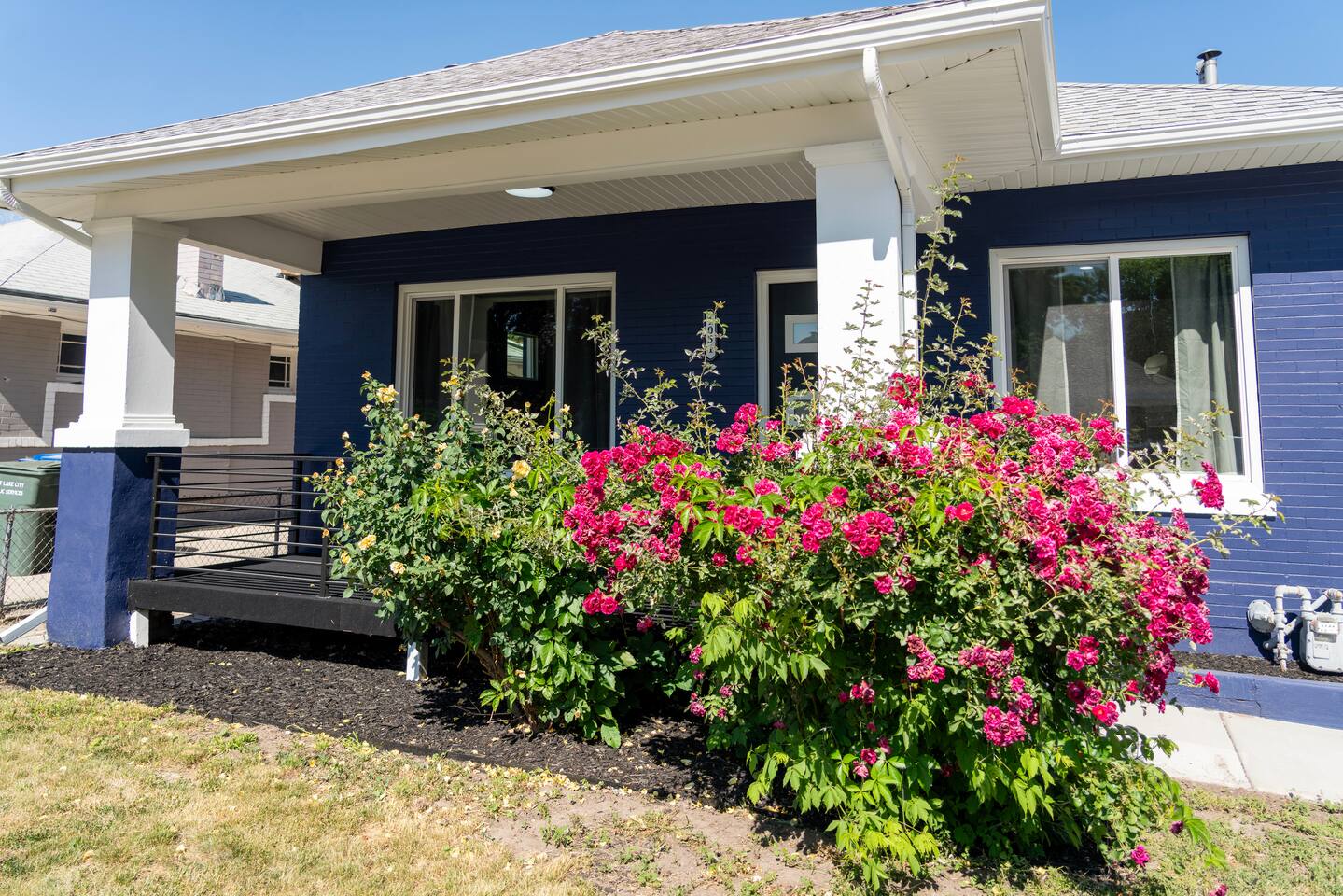 Covered front porch and railing surrounded by flowering rose bushes.
