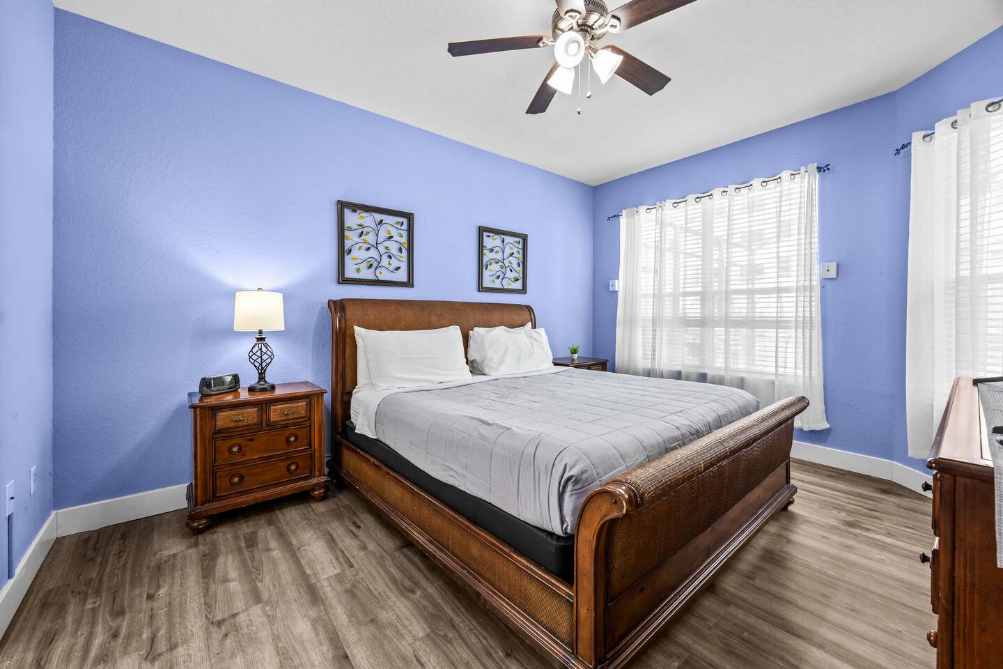 King bedroom with a wooden sleigh bed, botanical wall art, nightstand lamp, and 