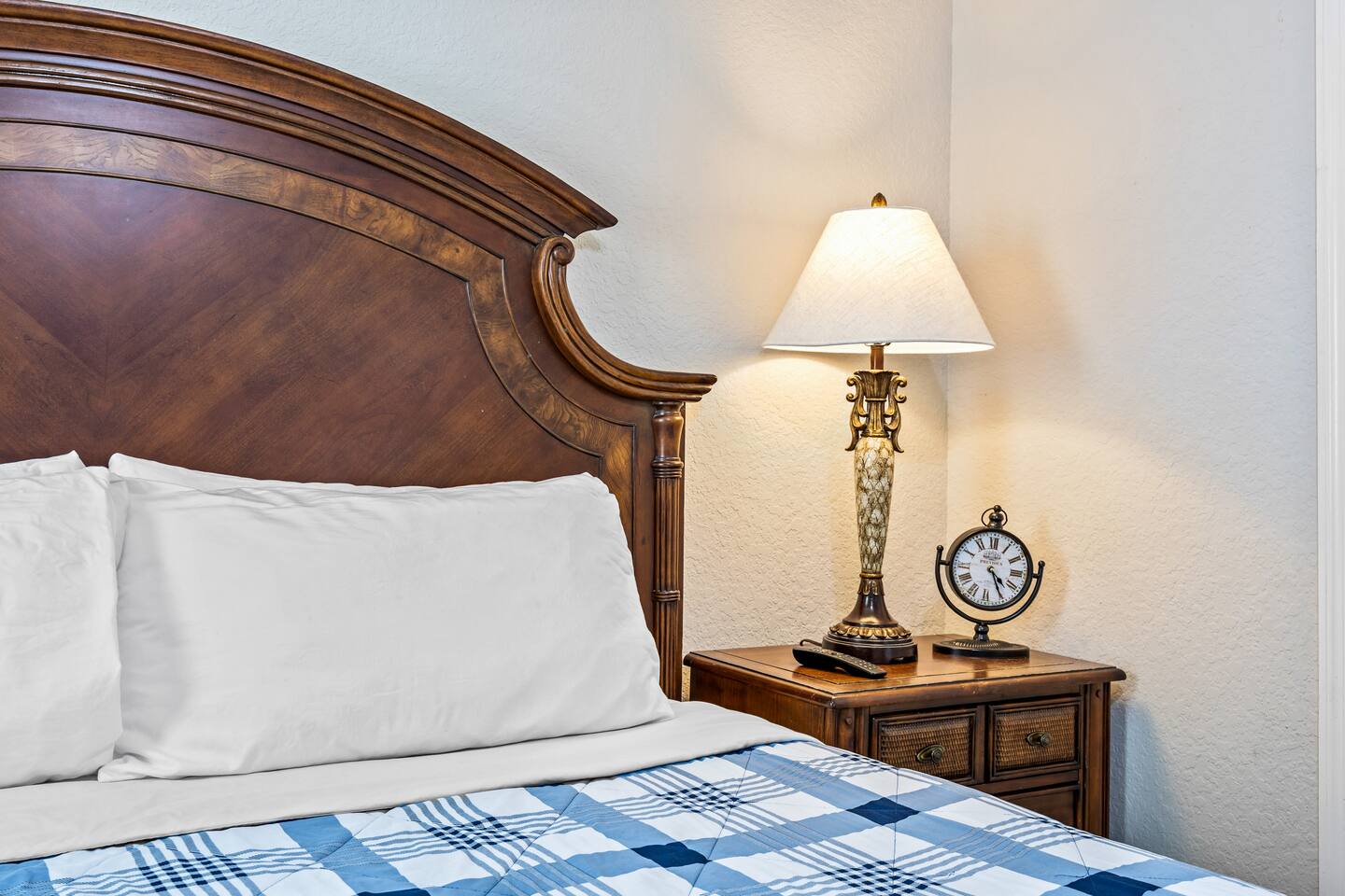Bedside detail with a carved wooden headboard, table lamp, and vintage-style clo