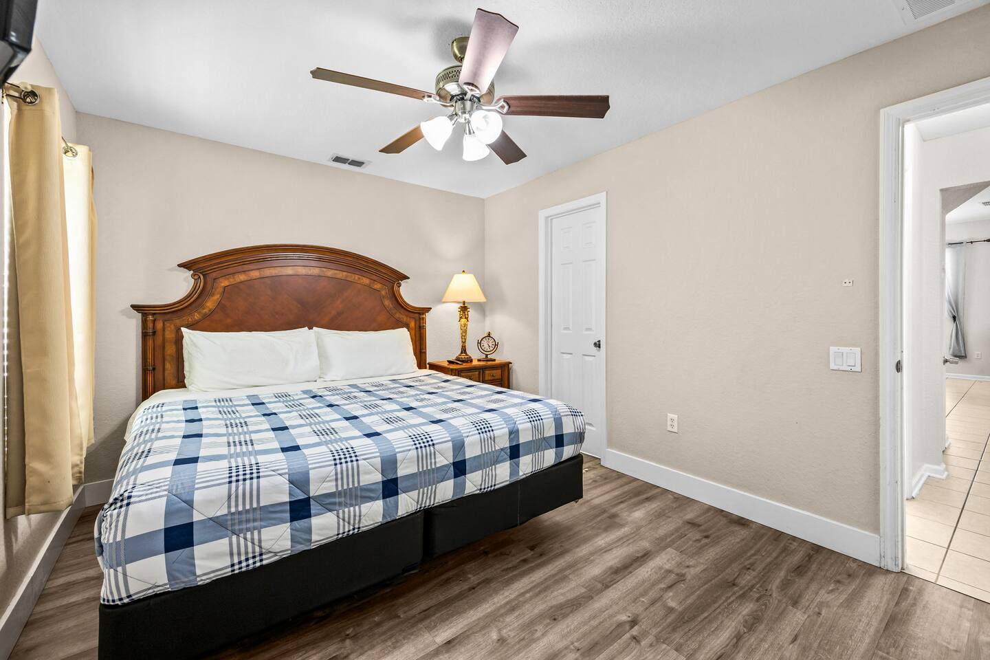 King bedroom with a carved wood headboard, plaid bedding, and neutral tan walls.