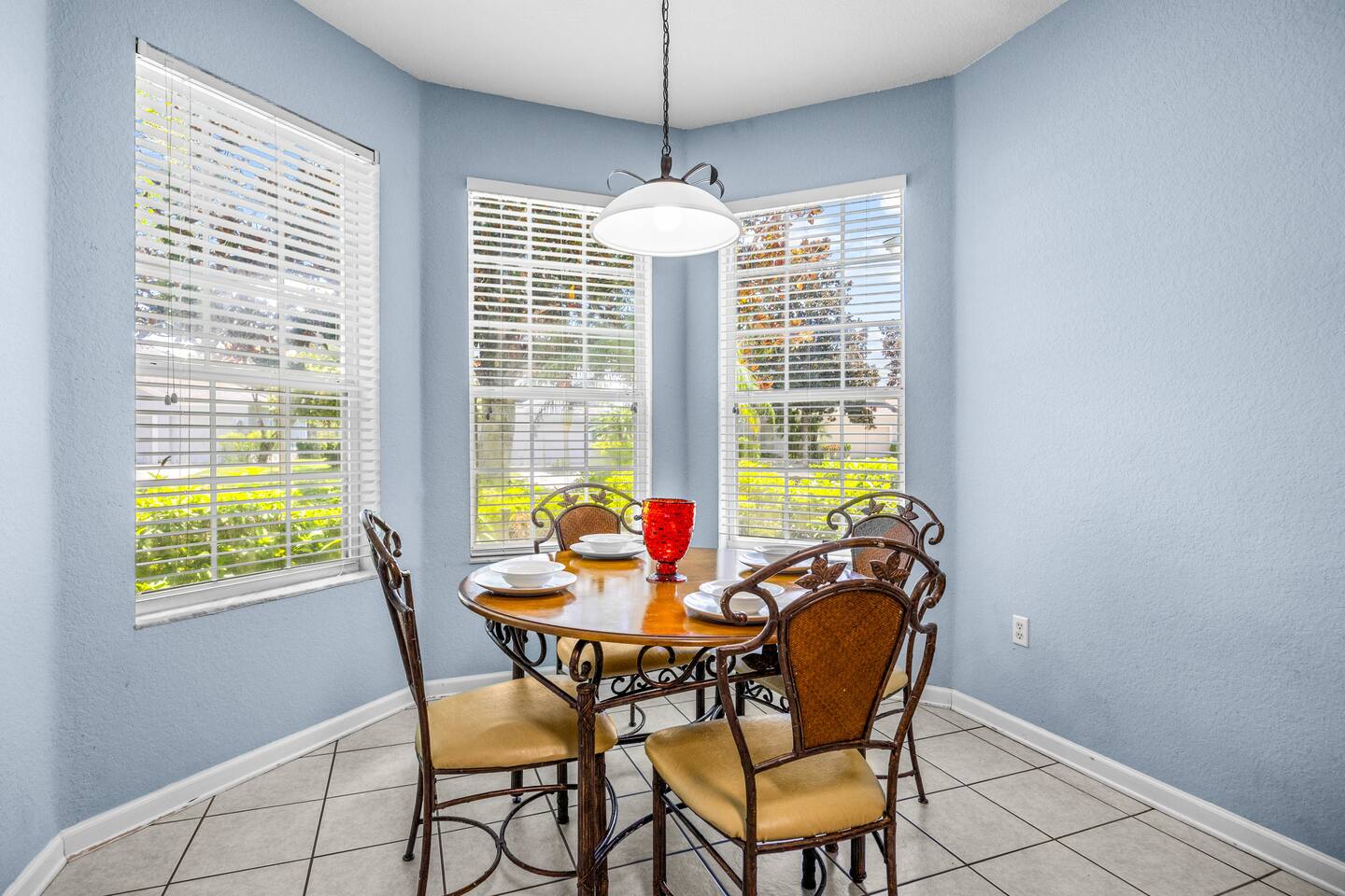 Breakfast nook with a round table, four chairs, and bay windows with blinds.