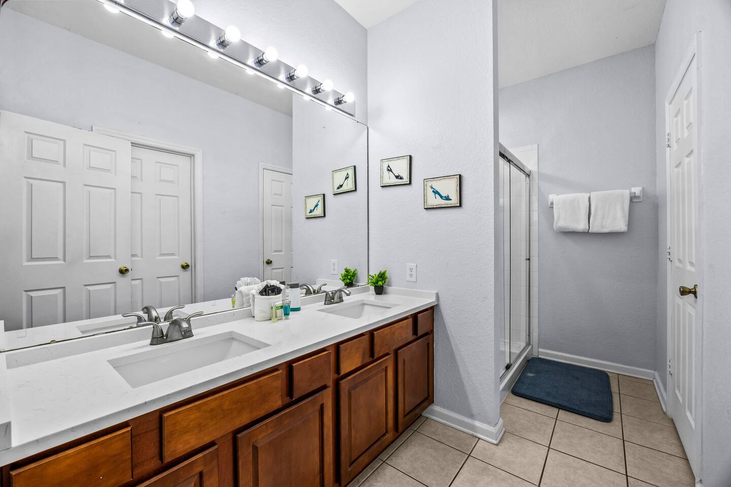 En-suite bathroom with a double vanity, framed artwork, and glass-door shower.