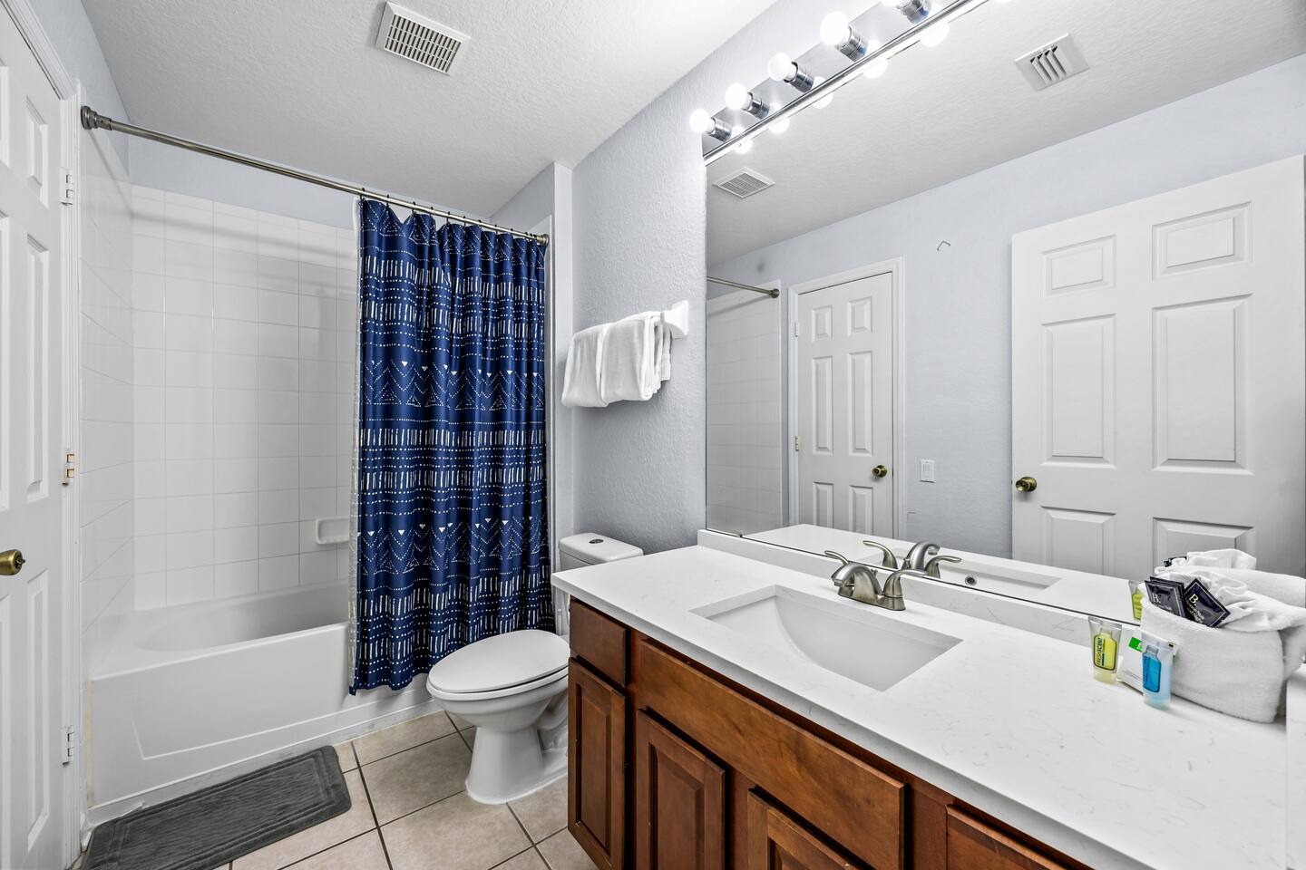 Bathroom with a tub/shower combo, patterned curtain, single vanity, and toilet.