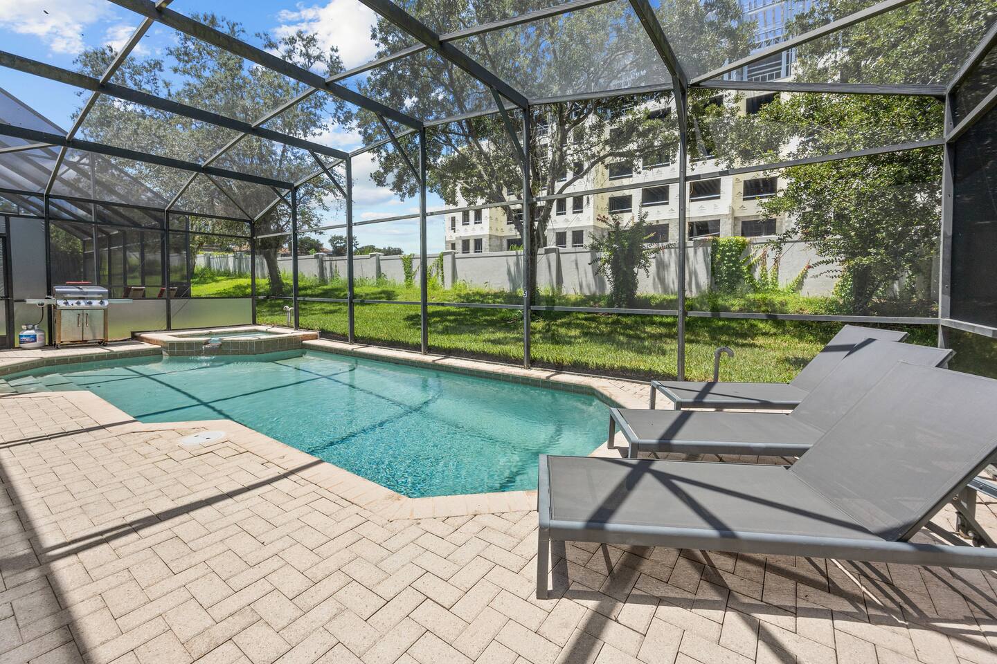 Screened private pool and spa with sun loungers and a gas grill, backing onto gr