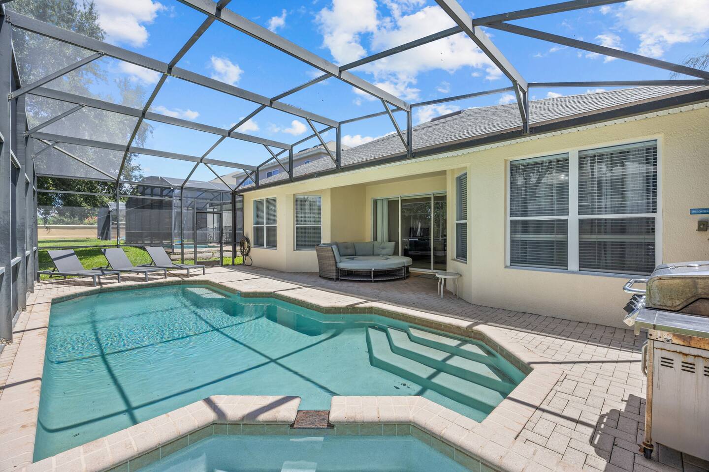 Private screened pool and spa with paver deck, loungers, and rear view of the ho