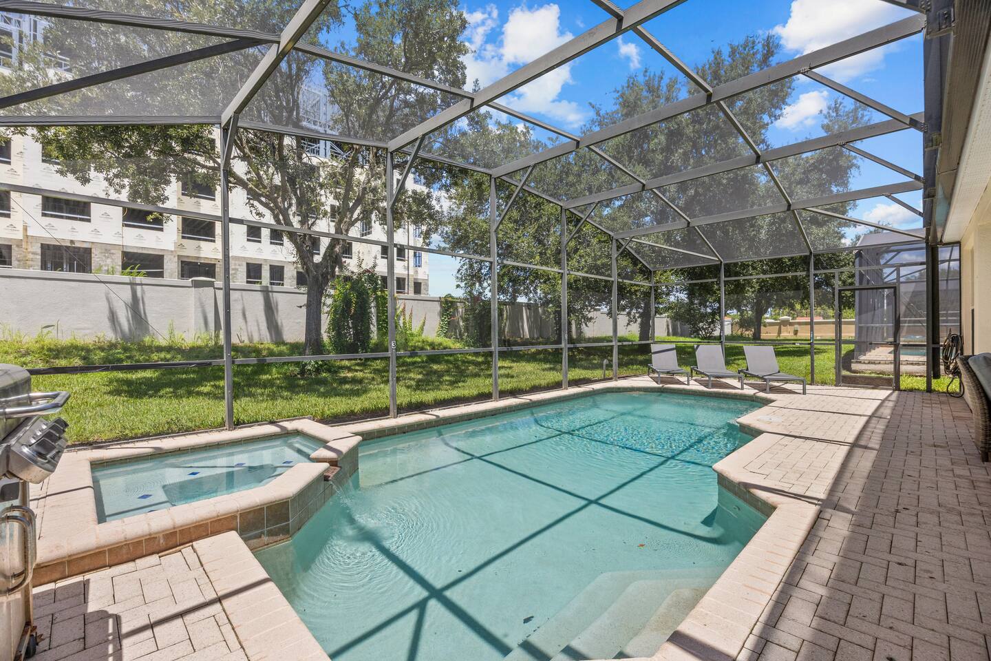 Screened private pool and attached spa with surrounding paver deck and lawn.